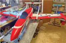Red and white model airplane with stars, in a cluttered workshop.