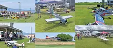 Remote-controlled planes on grass, people setting up, clear sky.